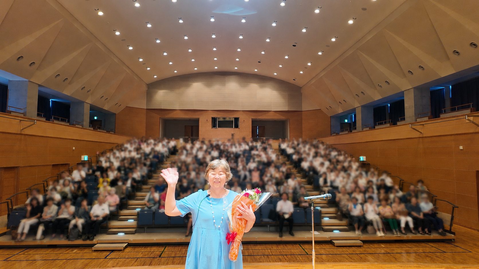 満席の講演会場で花束を手に手を振る野原広子